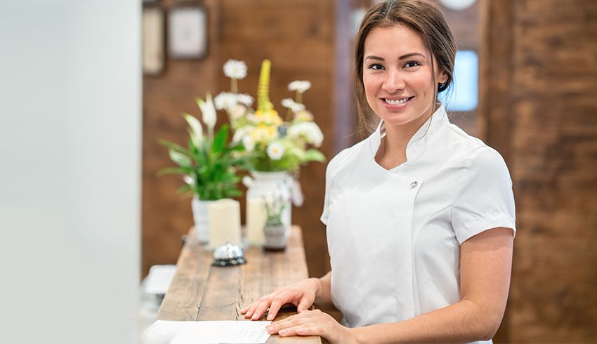 Female esthetician smiles behind front desk