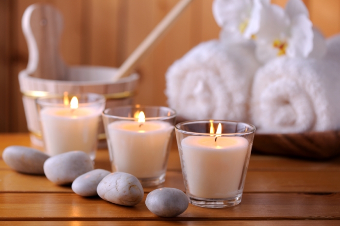 A close-up of a row of three candles in glass votives behind a row of decorative river stones set on a ledge in a cedar sauna.